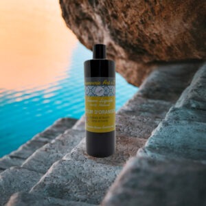 Savon liquide parfum Fleur d’Oranger 500 ml posé sur roche près de la mer, bouteille noire avec étiquette jaune et bleue.