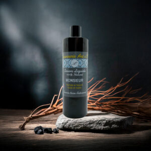 Flacon de savon liquide noir “Monsieur surgras” sur pierre, label bleu et doré, cadre rustic et fibres végétales en arrière-plan.