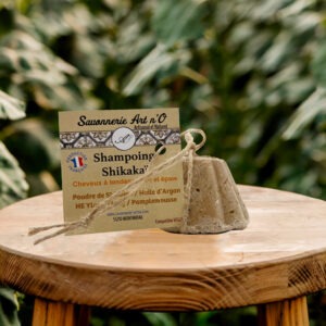 Shampoing Shikaka naturel et sachet d’épices ayurvédiques posé sur un rondin de bois, fond greenery.