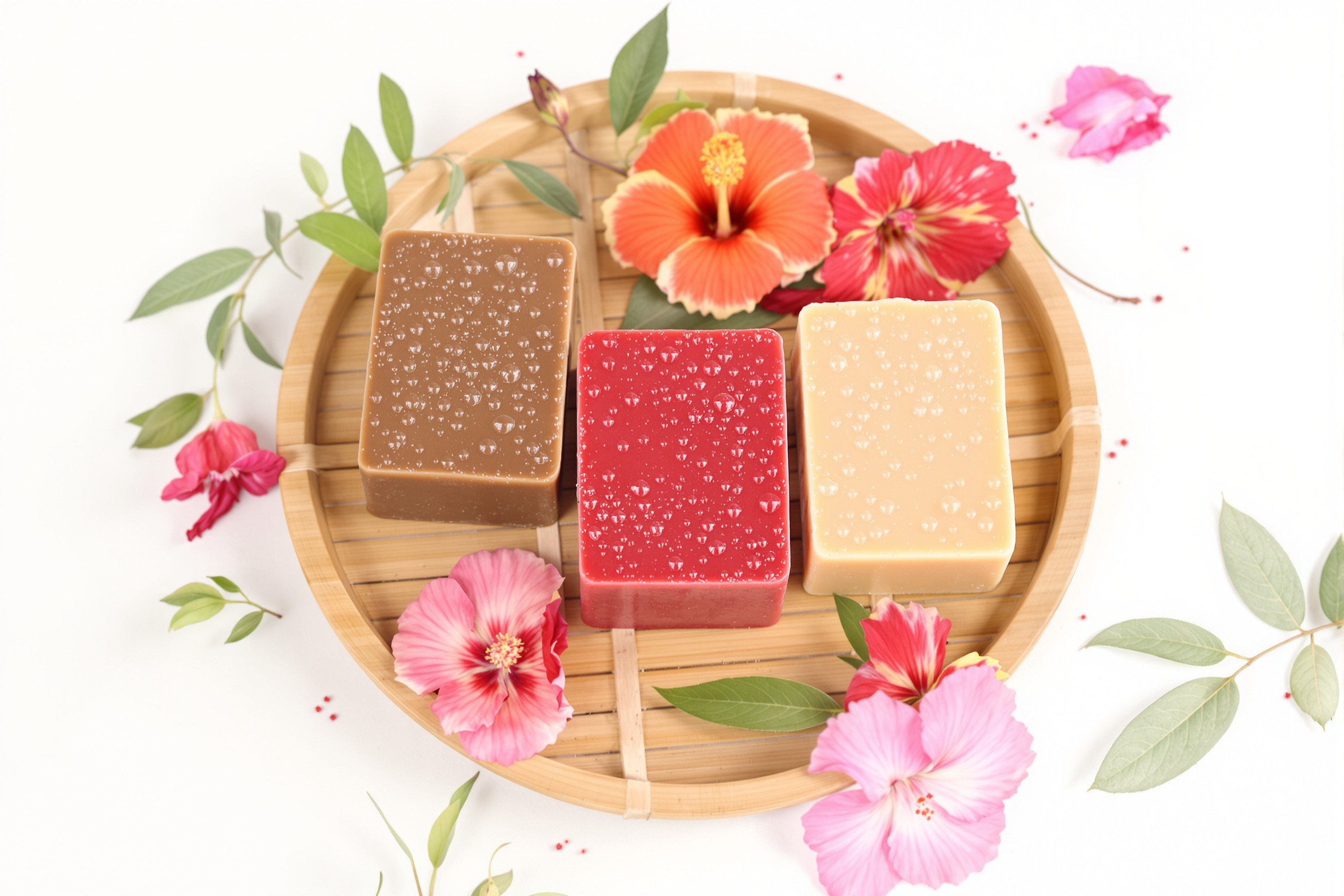 Savons solides colorés posés sur bambou avec fleurs hibiscus et feuillage, ambiance naturelle et colorée pour soins capillaires ayurvédiques bouclés.