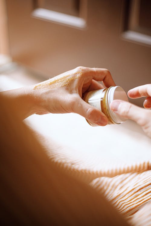Application d’une crème ou huile sur la main, présentaion d’un petit pot d’huile essentielle sur des draps.
