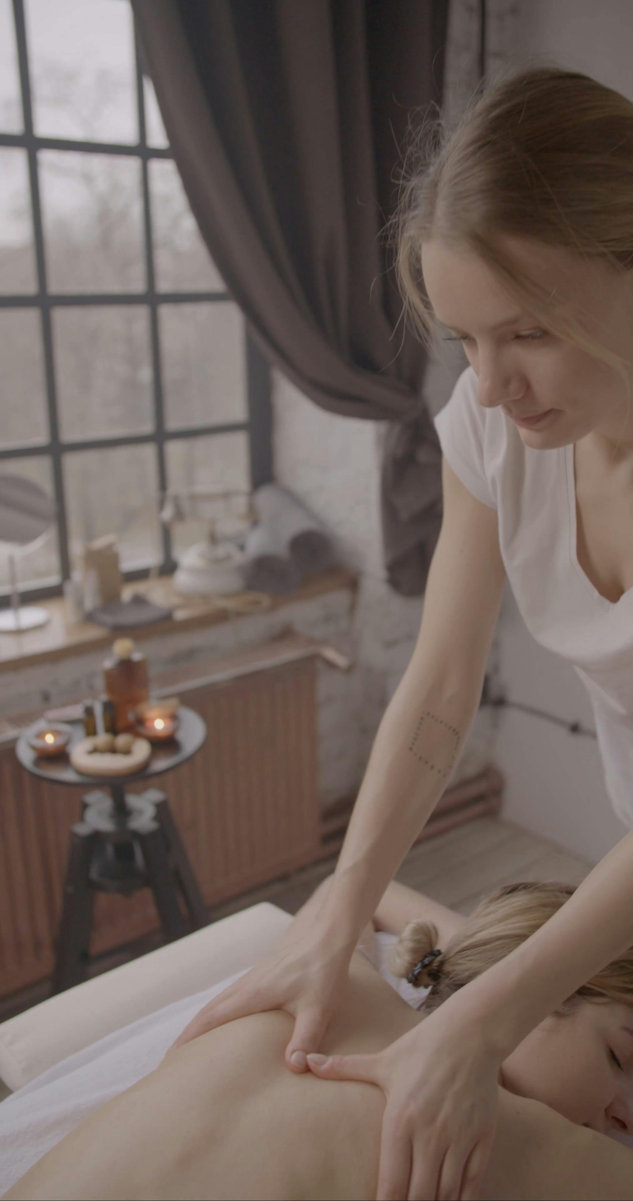 Massage relaxant sur le dos d’une personne en spa/atelier, masseuse accroupie qui applique une pression sur le dos, ambiance chaleureuse et lampes d’aromathérapie.